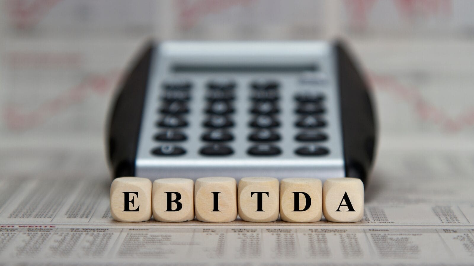 wooden blocks spelling EBITDA in front of a calculator