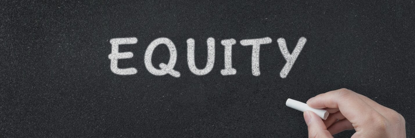 A person writing Equity on a chalkboard