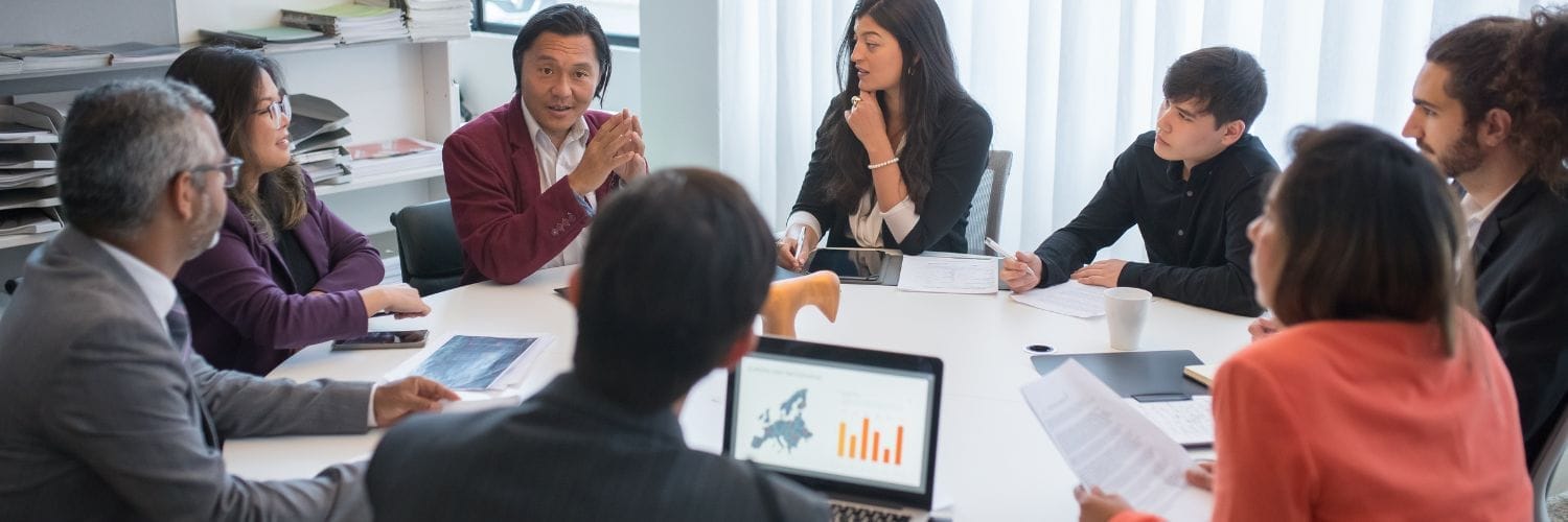 a group of people dressed professionally at a meeting looking at one person speaking