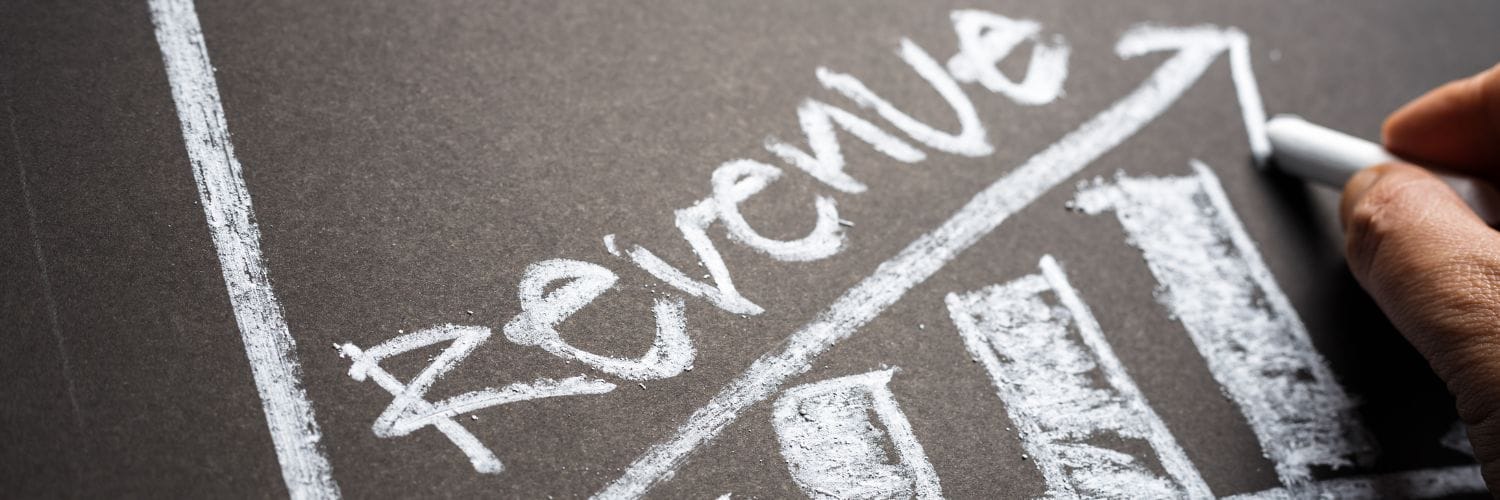 A hand writing on a chalkboard with the word revenue