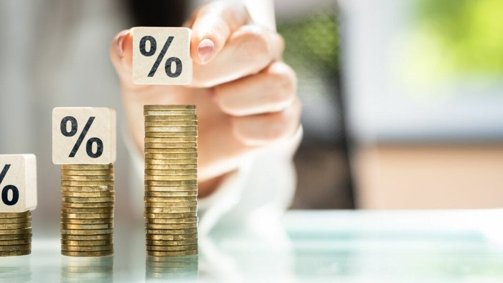 A person stacking blocks with a percent symbol  on top of coins of higher and higher stacks